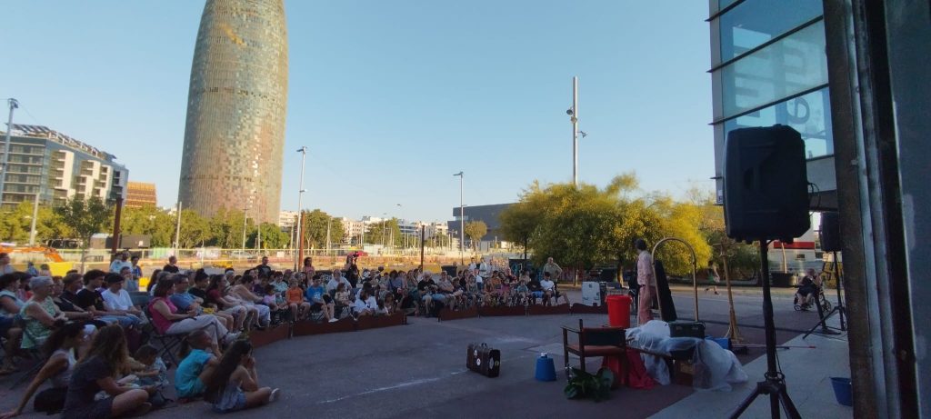 El Flaco, de El Flaco Circus, actuando al aire libre frente a un numeroso público en Barcelona, con la Torre Glòries al fondo.